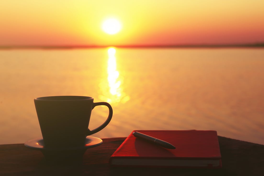 Cup of Coffee and Notebook on Sunset Background